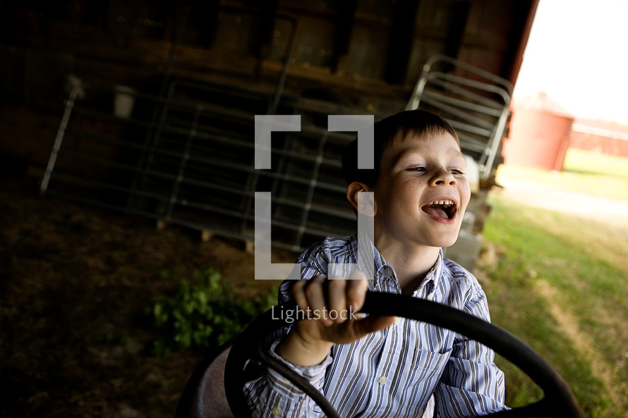 happy boy child with his hands on a tractor steering wheel 