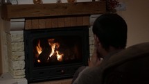 a man sitting in front of a fireplace talking on a cellphone 