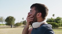 Man With Headphones Yawns Drowsily In Public Park