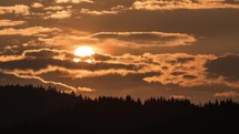 Orange sky with sun and clouds moving at sunset over forest Time lapse
