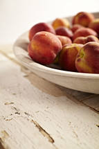 A bowl of peaches sit on an old wooden table.