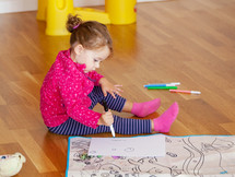 Two-year-old girl draws and colors on the floor at home