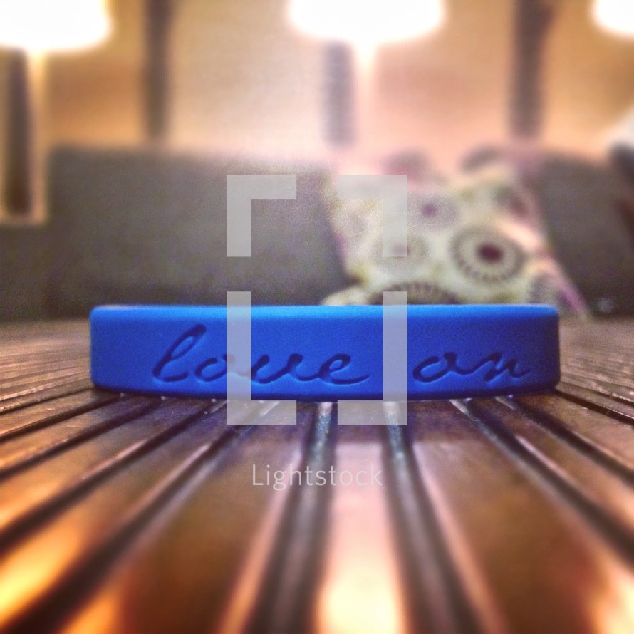 Blue Love On bracelet sitting on wood slat table with lights and pillows in the background.