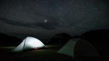 Night camping in illuminated tent under starry sky Time lapse
