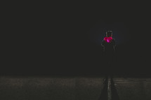silhouette of a boy standing in darkness holding a red glowing heart 