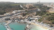 A pull back reveal 4k aerial drone footage of the harbor and cityscape of the city of Gozo, Malta along the coast of the Mediterranean Ocean.