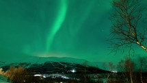 time-lapse of the aurora borealis with clouds moving over a mountain and city lights at night 