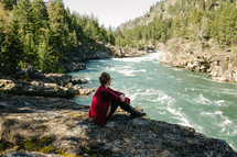 a woman sitting on a riverbank looking out at the rapids