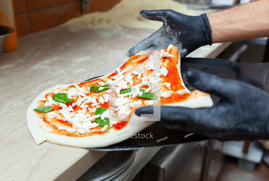 Raw margherita pizza put on baking shovel for cooking.