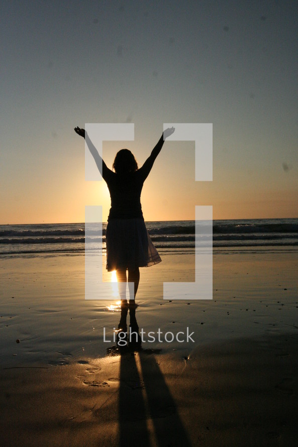 Woman on beach with hands raised to the sky