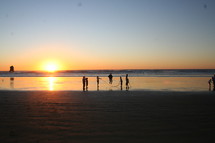 People playing jump rope on beach at sunset