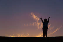 silhouette of a girl child with raised hands at sunset 