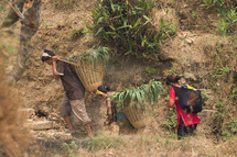 a family of farmers carrying crops in baskets on their backs 