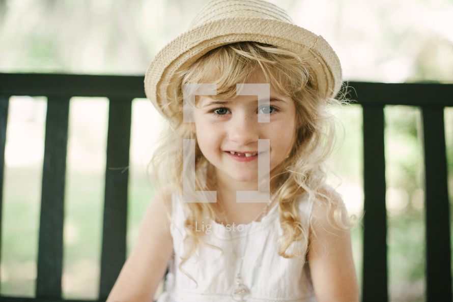 smiling girl child in a straw hat sitting on a bench 