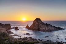 An ocean sunset and a rocky shore.