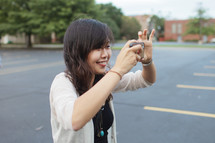 A woman standing in a parking lot taking a picture with a cellphone 