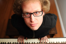 A man in glasses at a piano keyboard.