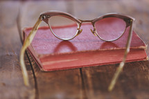 Eye glasses on an old book, which is on a rugged wooden table.