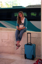 a woman sitting on a wall with luggage waiting 