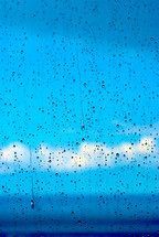 Blue sky and clouds seen through a window covered in raindrops.