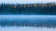 Mist on the lake with reflection of the tree line.