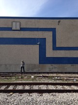 man standing in front of a warehouse near railroad tracks