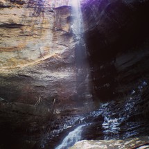 Sunlight beaming through limestone cavern with water running through it.