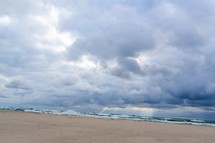 A sky full of clouds over a beach and ocean waves.