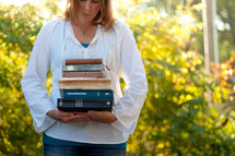 woman holding a stack of books outdoors 