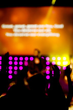 Silhouette of people with hands raised facing lighted stage during worship service