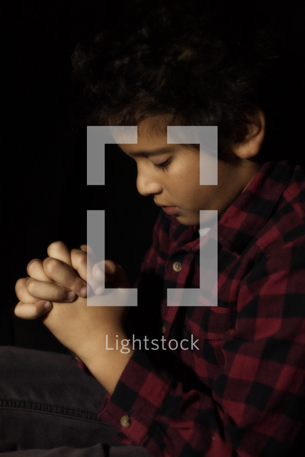 little boy with his fingers laced in prayer to God