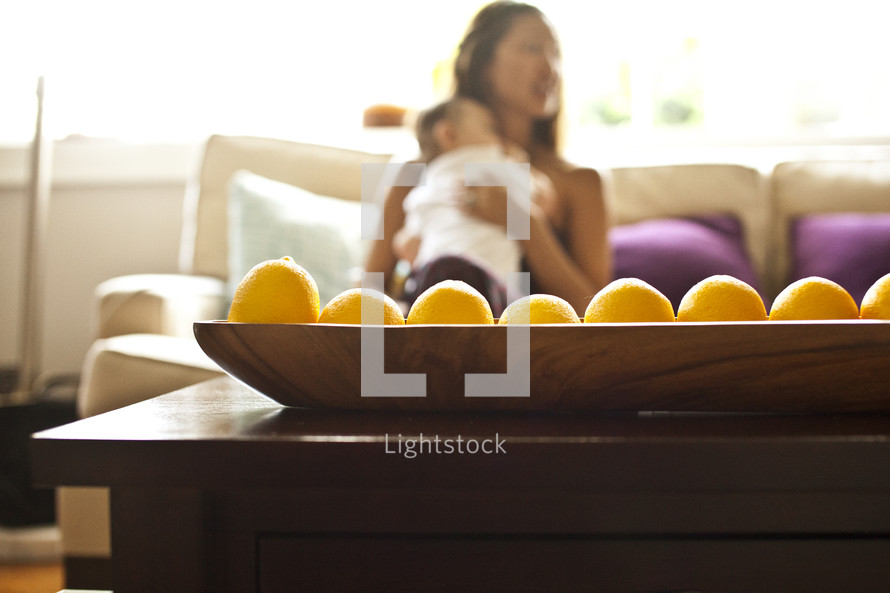 bowl of fruit on table - mother holding baby in background