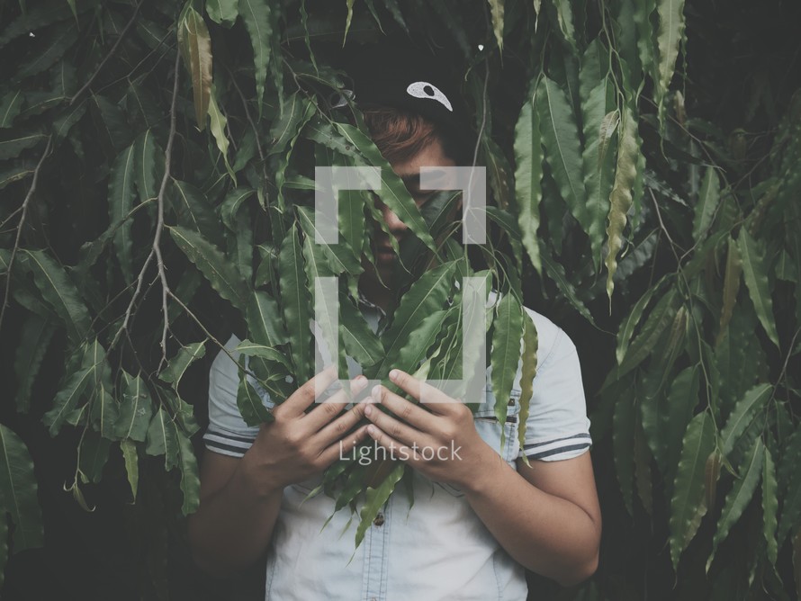 a teen boy hiding in green leaves on a tree 