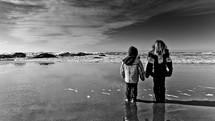 Children in jackets standing on water at the beach.