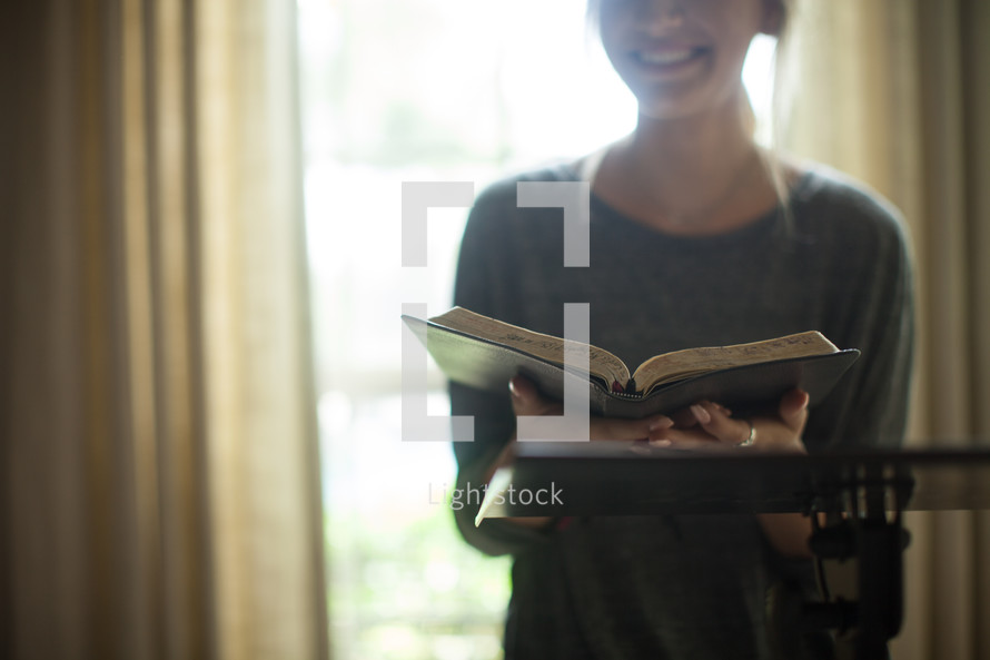 A smiling young woman holding an open Bible.