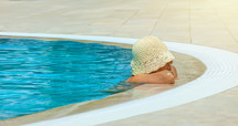 Woman in a stylish sun hat lounges in a refreshing pool, enjoying a peaceful moment of relaxation in the sunny outdoors