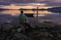 man sitting on a rocky shore at sunset 