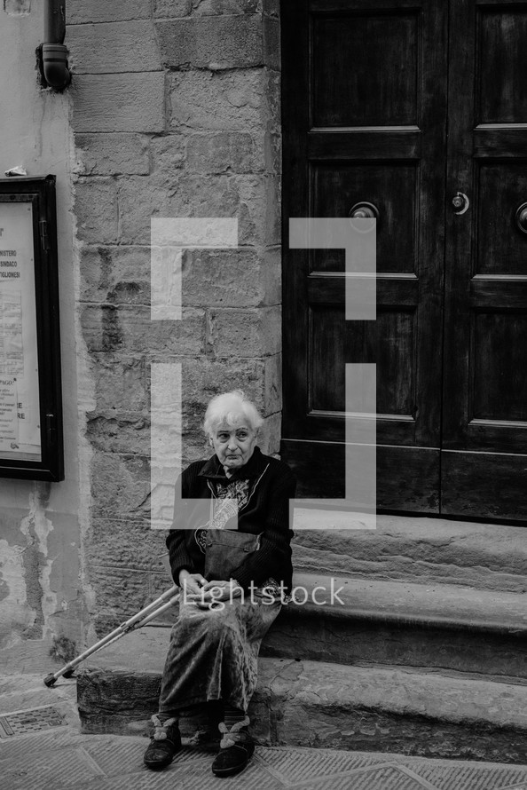 an elderly woman sitting on stone steps outdoors 