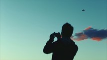 man with a camera taking a picture of a plane in flight 