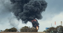 Accident in oil refinery - huge explosions and fireballs rising as thick black smoke covers the sky.