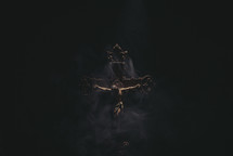 Dark and moody Jesus on a wooden cross with smoke and dramatic lighting.