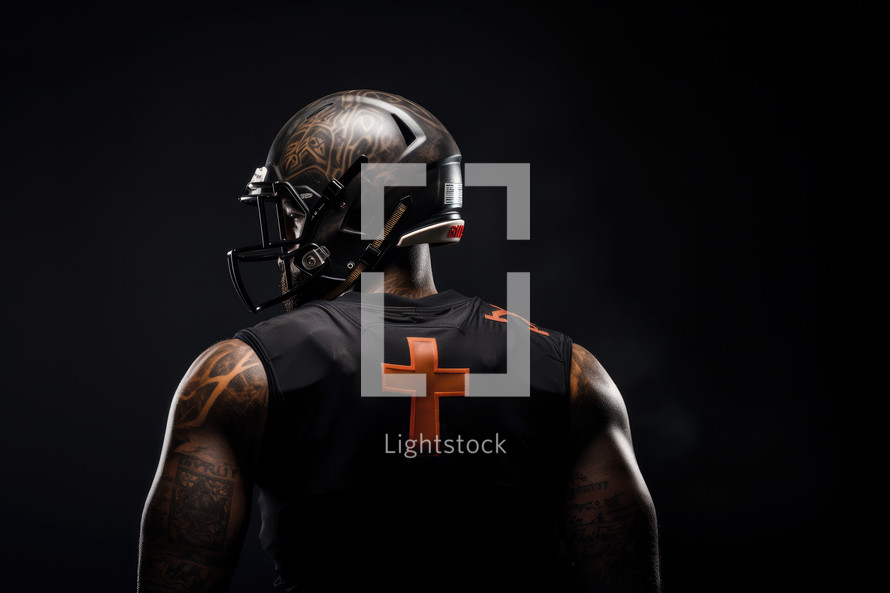Team Jesus. American football player with cross on his back, tattoo on his arms and helmet on black background