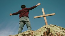 a man with outstretched arms standing in front of a cross 