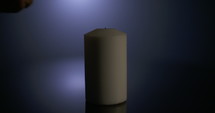 Slow motion macro footage of a white candle lit by a match on a dark background