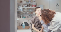 Female doctor examining a young boy's throat using an otoscope in the clinic.