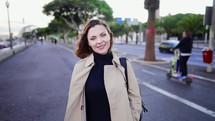 Portrait of cheerful woman standing on city street with backpack on shoulder. Female student or businesswoman smiling to camera. High quality 4k footage