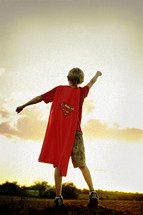 A boy in a superman cape with arms outstretched.