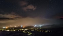 Stars with milky way and waves of misty clouds over night village Time-lapse
