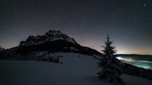 Night sky with stars moving over mountain peak in winter astronomy time lapse
