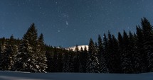 Blue starry night sky with stars moving over in winter forest mountains Astronomy time lapse
